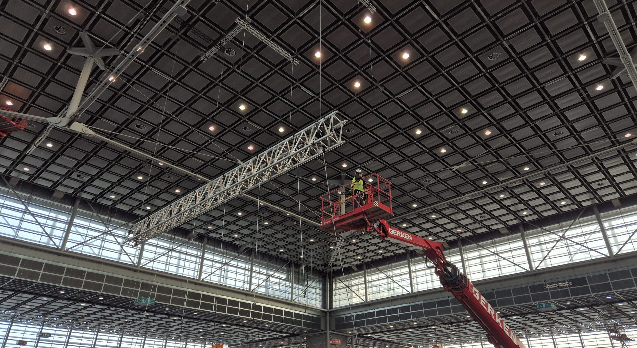 Messe Aufbau, Veranstaltungstechniker auf Steiger beim Einhängen einer großen Traverse in Decke der Messehalle